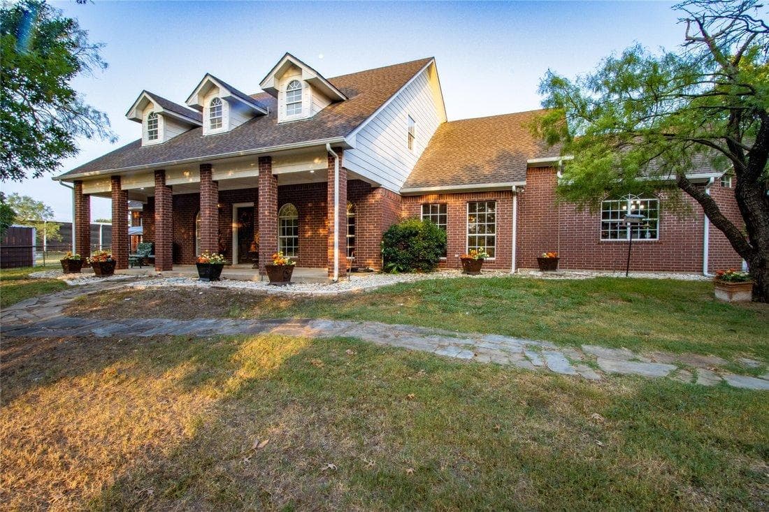 Large brick home featuring three dormer windows, a front porch, and a stone walkway.