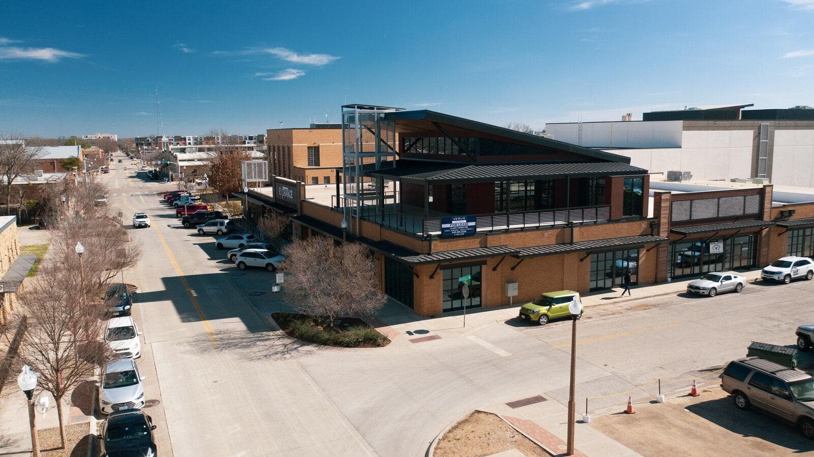 Modern two-story brick building with a slanted roof on a sunny city street corner.